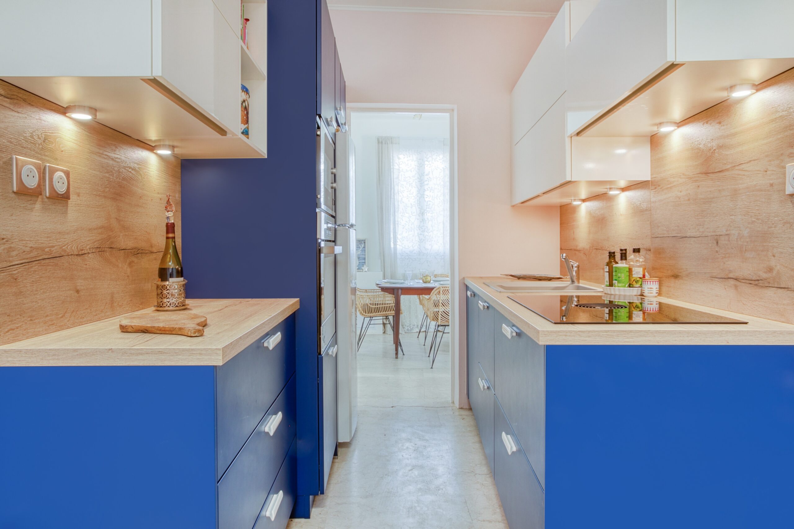 Cuisine Bleu : entre les deux lignes de meubles, un passage mène à la table du coin repas.