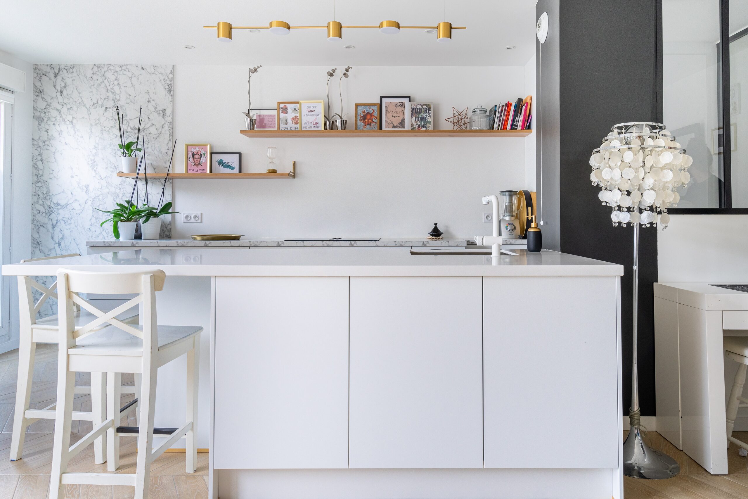 Cuisine Blanche : le débord de l’îlot au premier plan laisse de la place aux jambes côté tabourets.